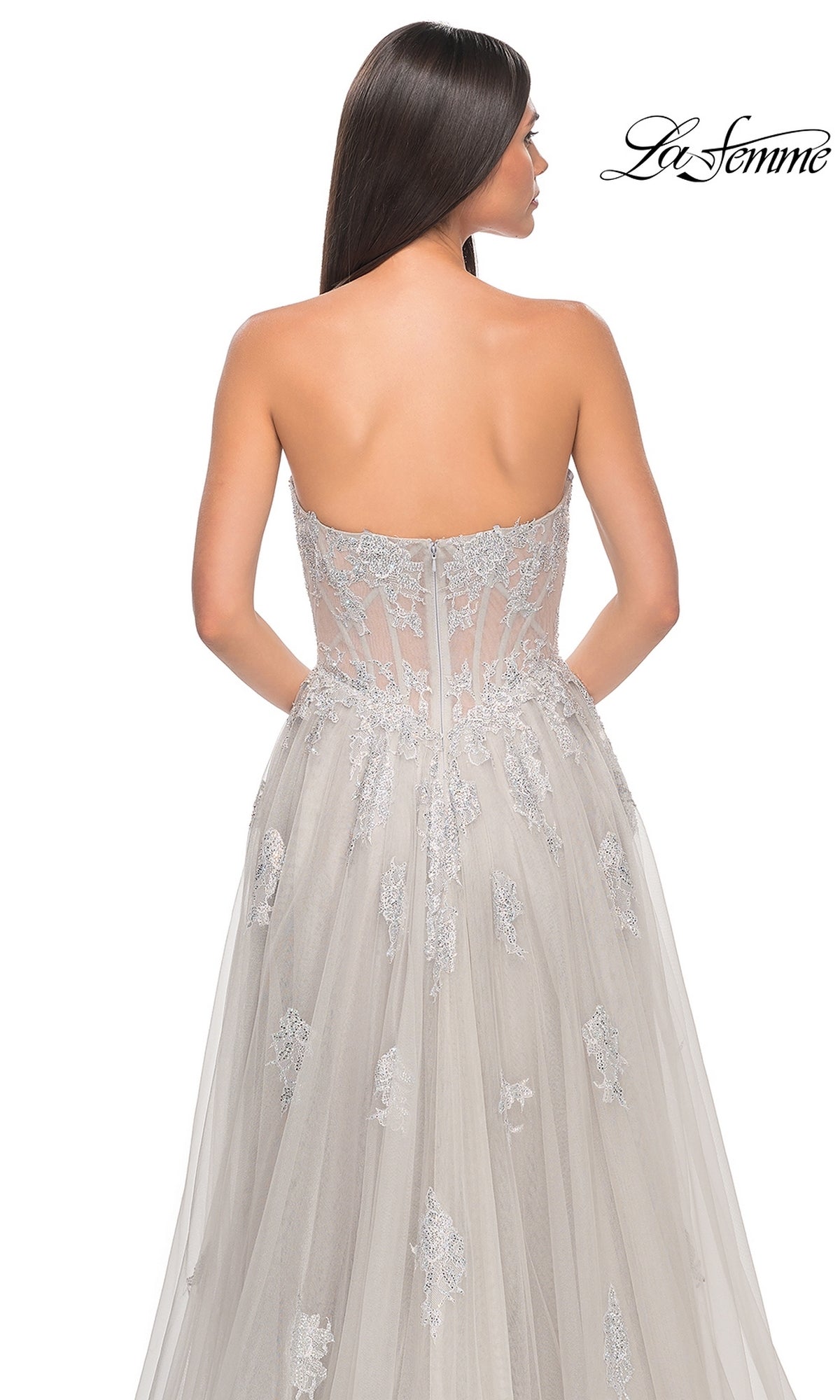 A woman with long brown hair models the La Femme Strapless Long A-Line Prom Dress 32111 in light gray, featuring embroidered-lace appliques and tulle, shown from the back with the La Femme logo in the top right corner.